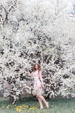 Güzel genç kız ile bukleler bir havada renkli elbise bir çelenk ile kafasındaki bir kiraz çiçeği Parkı güneşli bir günde yürüyüş