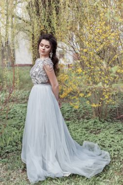 Güzel genç ihale gay kız ışığı elbiseyle bembeyaz bir gülümsemeyle bir güzel düğün saç modeli ile bir bahar Çiçek bahçesinde yürüyor
