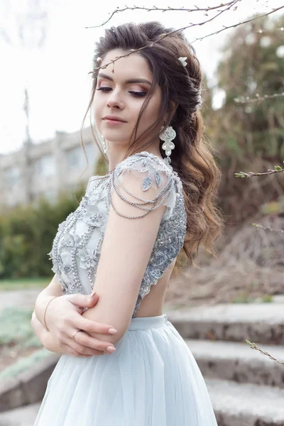 Güzel genç ihale gay kız ışığı elbiseyle bembeyaz bir gülümsemeyle bir güzel düğün saç modeli ile bir bahar Çiçek bahçesinde yürüyor — Stok fotoğraf