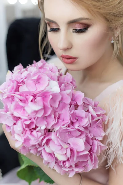 Matin d'une belle mariée tendre et douce dans une robe de boudoir avec un bouquet de fleurs d'hortensia avec une coiffure du soir et un maquillage lumineux en studio — Photo
