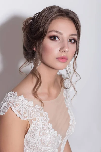 Portrait of a beautiful tender young bride with evening festive hair and gentle make-up in a snow-white dress with a train — Stock Photo, Image