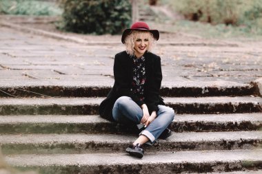 Palto ve şapka sokakta merdivenlerde oturan kısa kıvırcık saçlı güzel neşeli sarışın kız