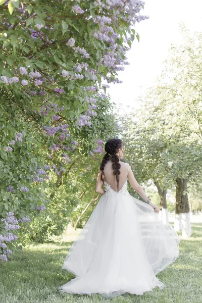 Leylak parktan bir güneşli bahar gününde yürüyüş onun elinde bir buket beyaz hava elbiseli ihale güzel şirin kız gelin. Fotoğraf yumuşak renklerde — Stok fotoğraf