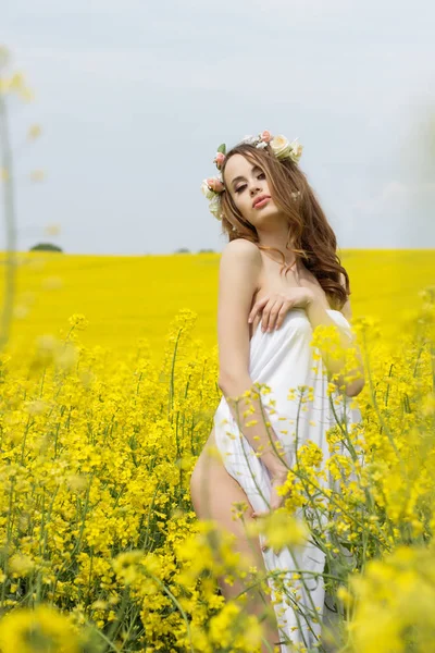 Beautiful sexy young girl with red hair in a field of yellow flowers covered with a white cloth — Stock Photo, Image