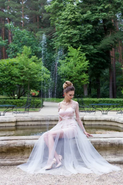 Beautiful elegant girl in evening dress with beautiful evening festive hairdo near fountain
