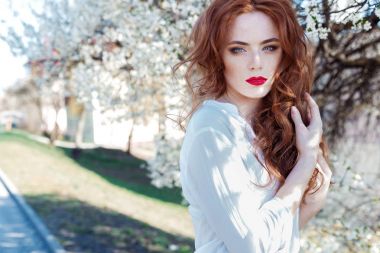 Çiller ile kentin açık güneşli bir çiçek açan ağaçlar yakınındaki dudaklarında kırmızı ruj ile güzel seksi Kızıl saçlı kız