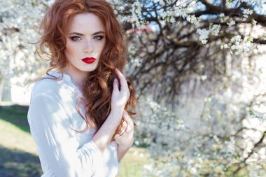 Çiller ile kentin açık güneşli bir çiçek açan ağaçlar yakınındaki dudaklarında kırmızı ruj ile güzel seksi Kızıl saçlı kız