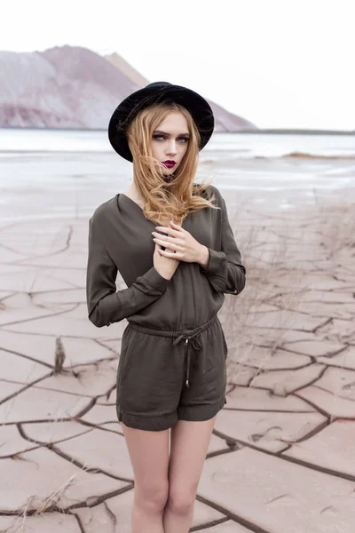 Mooi, sexy blond meisje poseren in de bergen op een gekraakt terrein in een zwarte hoed met lichte make-up — Stockfoto