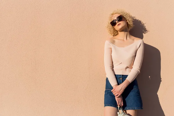 석양 햇빛에 벽 근처 선글라스 스탠드에 곱슬 머리와 아름 다운 젊은 여자 — 스톡 사진