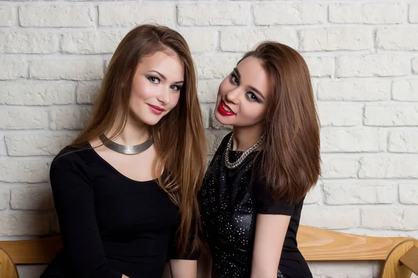 Dos hermosas chicas jóvenes en vestidos negros sentarse en el banco y chismorrear —  Fotos de Stock
