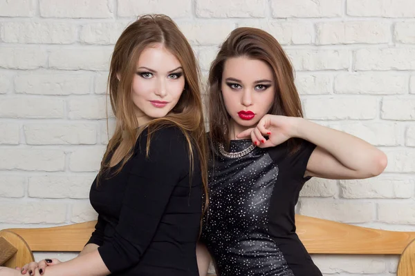 Zwei schöne junge Mädchen in schwarzen Kleidern sitzen auf der Bank und tratschen — Stockfoto