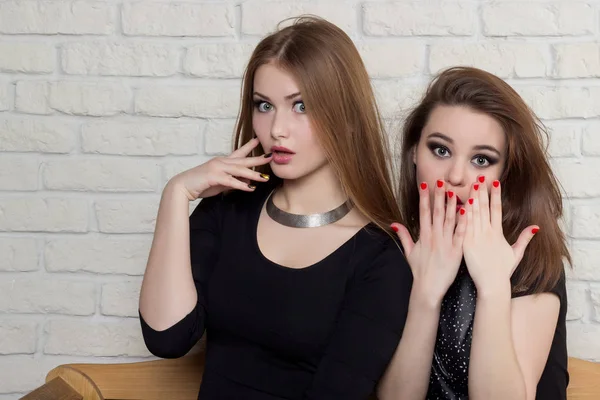 Дві красиві молоді дівчата в чорних сукнях сидять на лавці і плітках — стокове фото