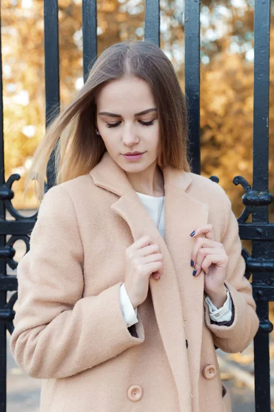 Beautiful young girl in the autumn foliage walks through the city streets on a sunny afternoon in a coat and a warm jacket — Stock Photo, Image