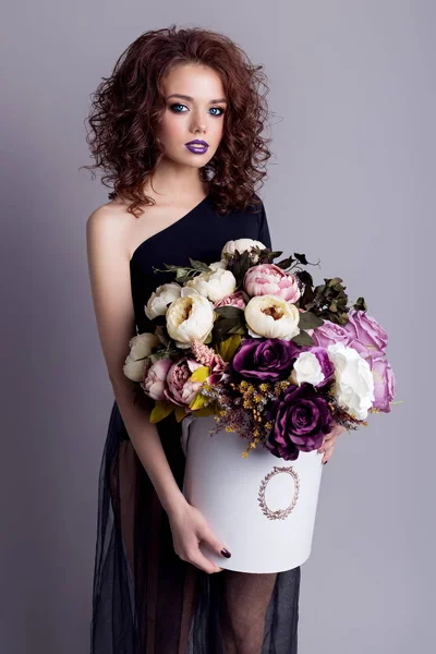 Beautiful sexy girl with plump lips in black body with a bouquet of flowers in the studio, evening hairstyle and makeup — Stock Photo, Image