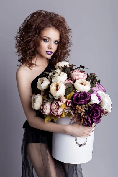 Beautiful sexy girl with plump lips in black body with a bouquet of flowers in the studio, evening hairstyle and makeup — Stock Photo, Image