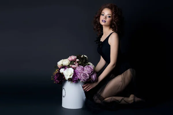 Сексуальная девушка с пухлыми губами в черном теле с букетом цветов в студии, вечерней прической и макияжем — стоковое фото