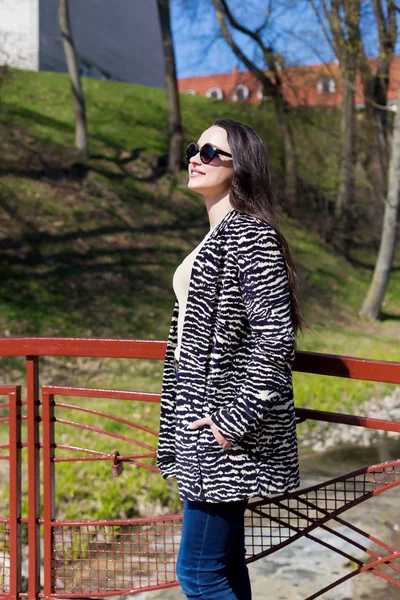 Красивая стильная девушка гуляет в парке в солнцезащитных очках ранней весной в солнечный яркий день — стоковое фото