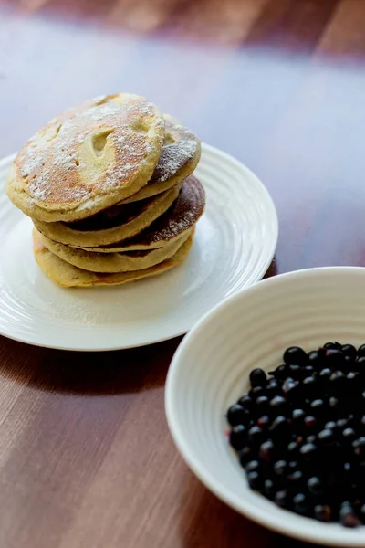 pancakes with berries and powdered sugar in a white plate are on the table
