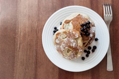 Masanın üzerinde böğürtlenli krep ve pudra şekeri var.