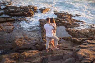 Joven pareja disfrutan de su amor frante una puesta sol en el mar