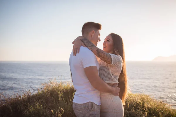 Joven pareja disfrutando de un paseo en una puesta de sol frante al mar