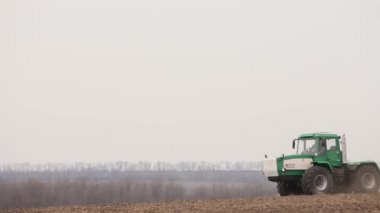 Yeşil traktör ve kırmızı ekiciler tarlayı sürüyor.