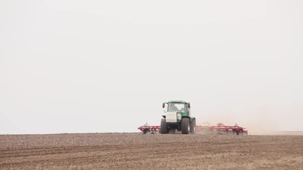 Groene trekker en rode cultivator ploegt de grond op het veld in het voorjaar — Stockvideo