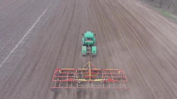 Luftaufnahme. Grüner Traktor und roter Grubber arbeiten im Frühjahr auf dem Feld — Stockvideo