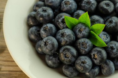 Masada yeşil yapraklı taze toplanmış ve sulu yaban mersinleri. Ahşap arka planda yabanmersini.