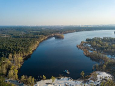 Bir şehrin eteklerindeki kozalaklı bir ormanda bir göl. Havadan