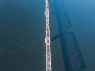 Hava aracı görüntüsü. Kiev 'deki Dinyeper Nehri üzerindeki demiryolu köprüsü. Köprünün gölgesi nehrin pürüzsüz yüzeyine düşüyor