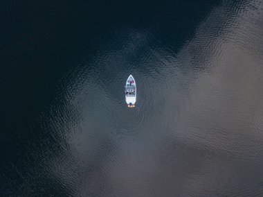 Teknede bir balıkçı. Bulutlar suya yansıyor. Hava aracı görünümü.