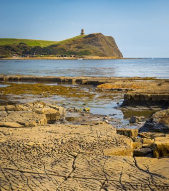 Bright sunlight illuminates sea, rocks and cliffs on Jurassic Co clipart