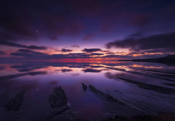 南ドーセットのジュラシック海岸線の深い赤と紫の雲を示すのに十分な長さの雨嵐の後に空がクリアされます — ストック写真