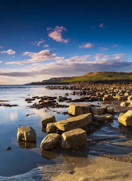 The low sun casts a golden glow onto the Jurassic cliffs and rocks of Kimmeridge Bay in Dorset
