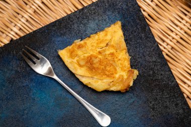 Mavi ve siyah arka planda beyaz tabakta patates omleti.