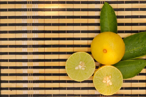 Top view of fresh lemon cut and raw yellow lemon with green leaves put on bamboo table