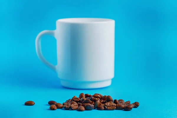 Hromada kávových zrn v přední části bílého umytého poháru na modrém pozadí — Stock fotografie