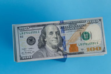 100 dolarlık banknot havada süzülüyor mavi bir arka planda.