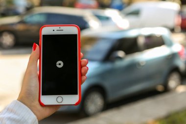 KIEV, UKRAINE - 1 Mayıs 2017: Uber mobil uygulamalar. Yolda ve mavi arabada Apple iPhone 'da Uber uygulamasını tutan bir kadın. Uber logosu. Taksi şoförü..