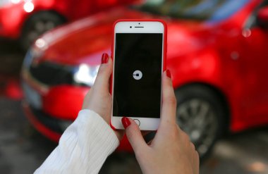 KIEV, UKRAINE - 1 Mayıs 2017: Uber mobil uygulamalar. Yolda ve kırmızı arabada Apple iPhone 'da Uber uygulamasını tutan bir kadın. Uber logosu. Taksi şoförü..