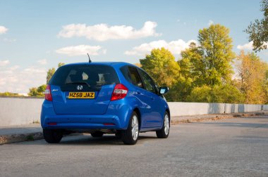 Londra, İngiltere - 20 Temmuz - Honda Jazz, sonbahar ormanının arka planına karşı yolda park etmiş mavi araba. Otomotiv fotoğrafçılığı. Mesaj için yer var. Arabayla arka plan. Özel şehir arabası Honda Jazz. 
