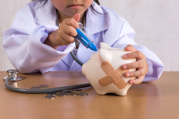 Menina asiática jogando como um médico cuidado Piggy Bank — Fotografia de Stock