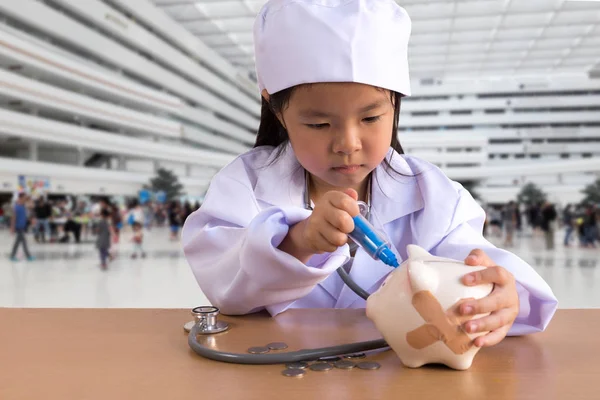 Menina asiática jogando como um médico cuidado Piggy Bank — Fotografia de Stock