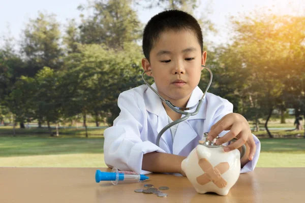 Asiático chico jugando como un médico cuidado piggy banco —  Fotos de Stock