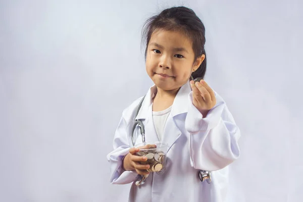 Asiático chica jugando como un médico cuidado dinero en taza —  Fotos de Stock