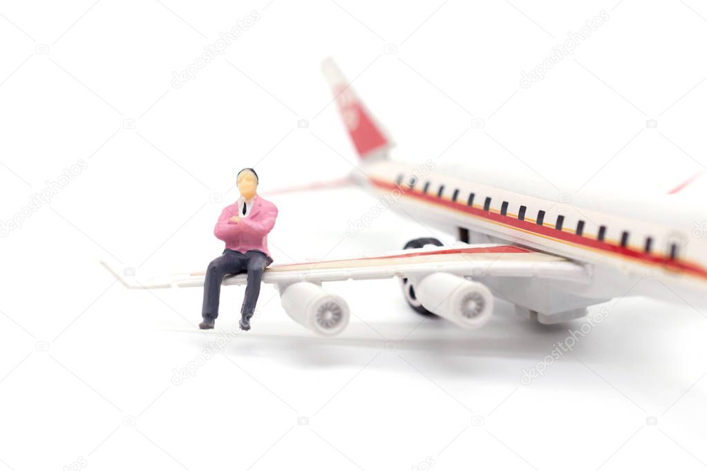 Miniature businessman sitting on airplane wing on white backgrou