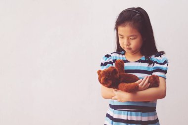 Asyalı kız oyuncak ayıya sarılıyor.