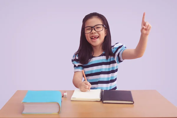 Niña asiática escribiendo un libro sobre la mesa. mostrar el dedo índice — Foto de Stock