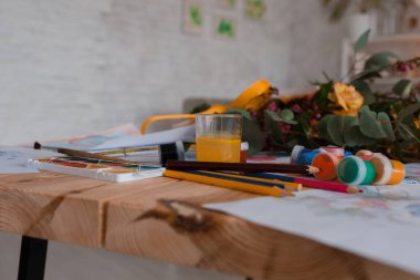 Suluboya boya, renkli kalemler, fırçalar, beyaz kağıt ve tahta bir masanın üzerindeki çiçek. Hobi olarak. - Sanat. Çocukluk. Seçici odaklanma. Orta keskinlikte